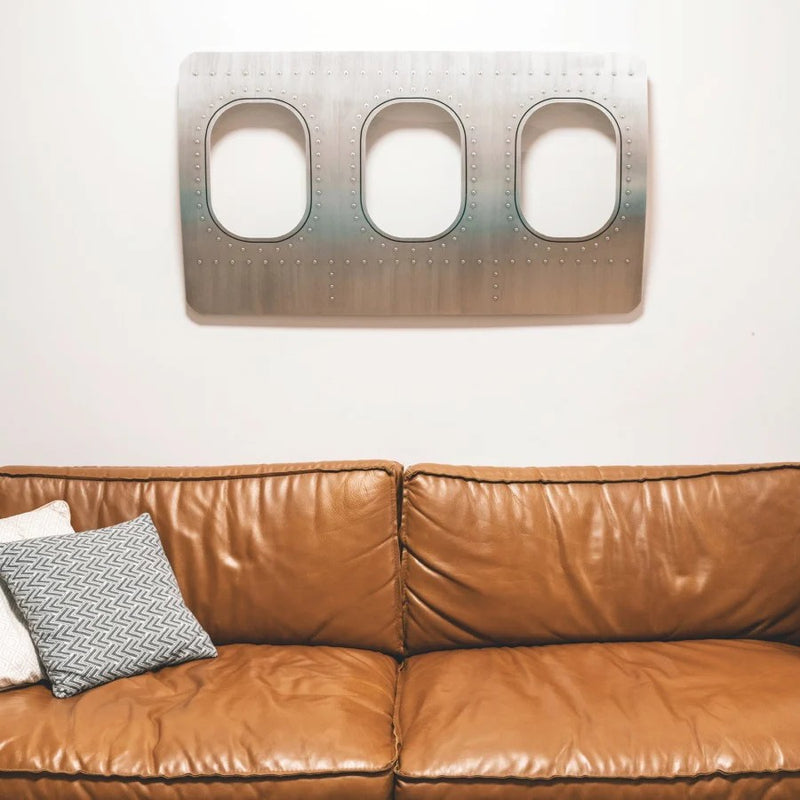 Flugzeugfenster als dekoratives Flugzeugmöbel über einem Sofa an der Wand montiert, stilvolle Geschenkidee im Aviation Design für Wohnräume
